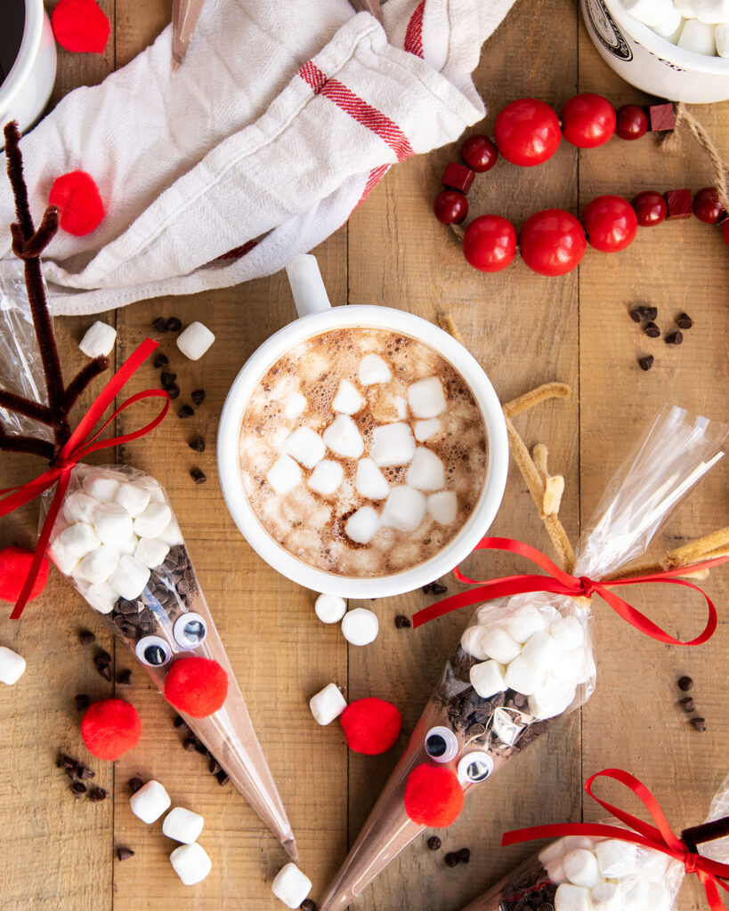 An above view of a cup of hot cocoa with marshmallows, and a hot chocolate bag full of cocoa mix, mini marshmallows, and chocolate chips.