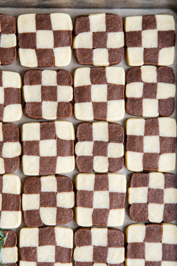 An above view of checkerboard cookies in rows all next to each other on a cookie sheet.