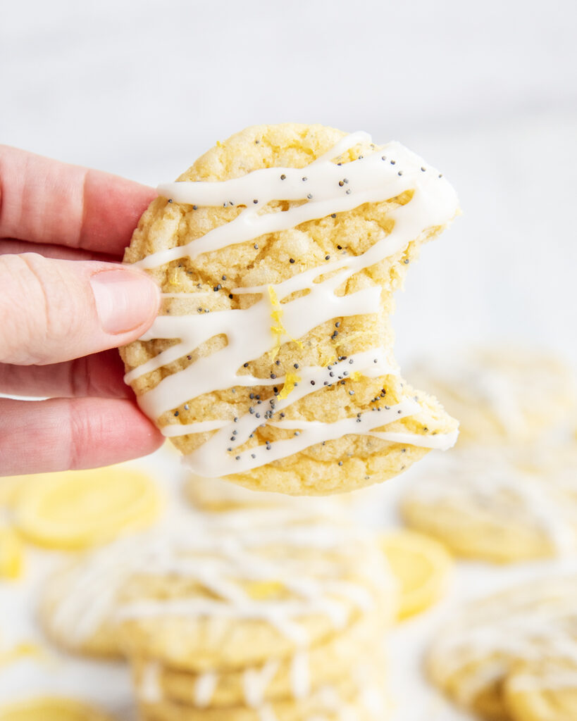 A hand holding a lemon poppy seed cookie with a bite out of it.