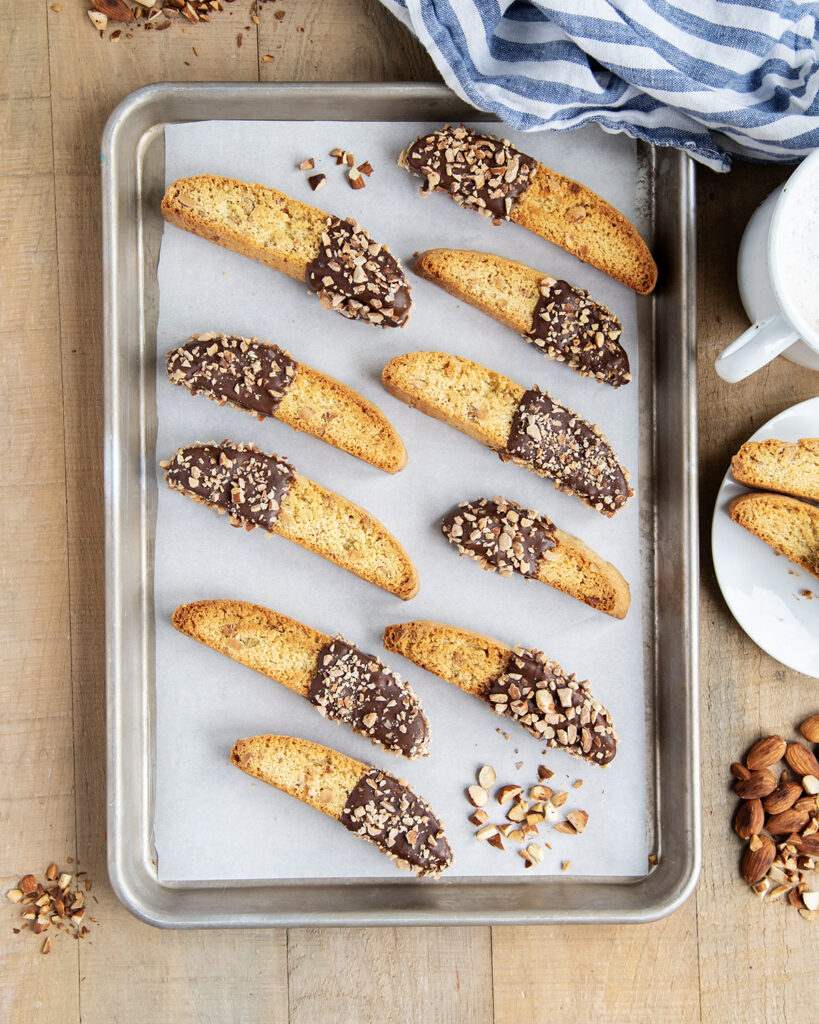 Rows of chocolate dipped almond biscotti on a parchment paper lined baking sheet.