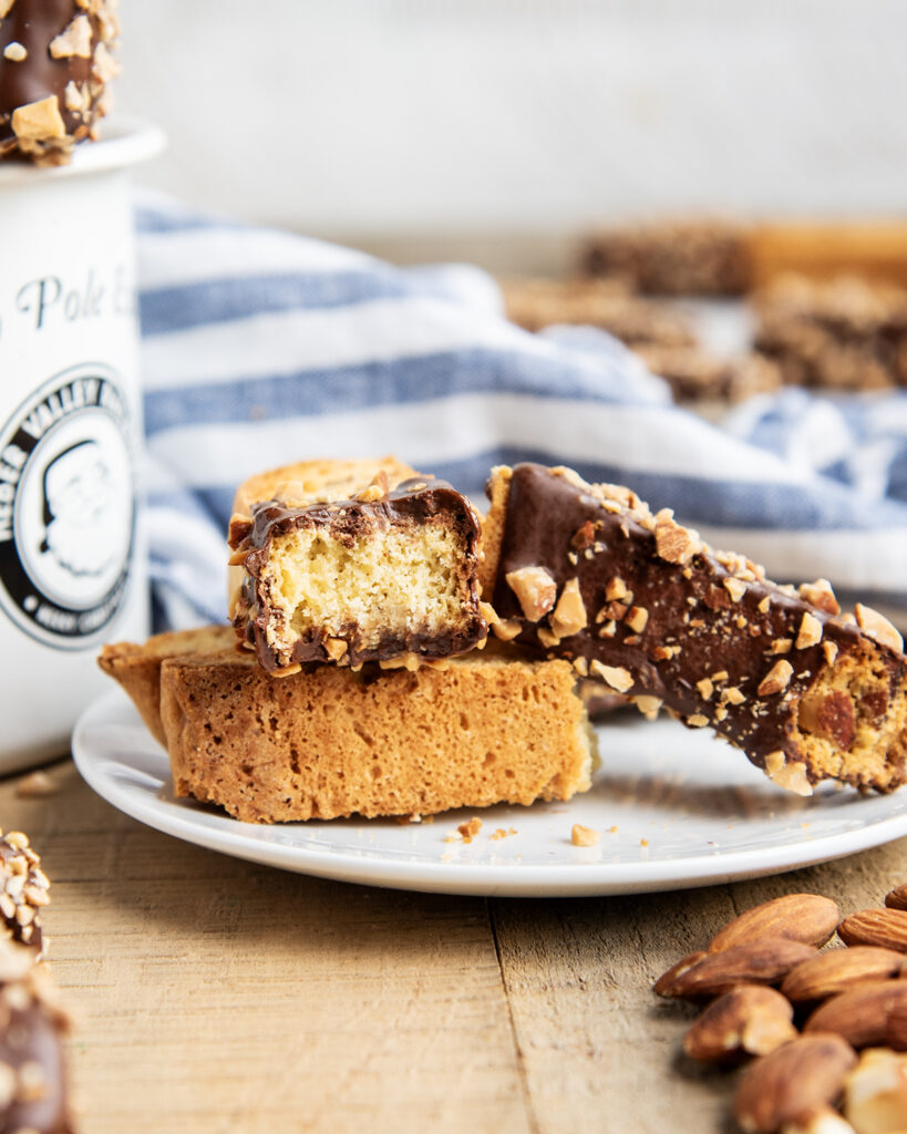 A plate of almond biscotti, dipped half in chocolate and one has a bite out of it.