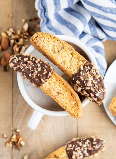 Two chocolate dipped almond biscotti on a mug of coffee.