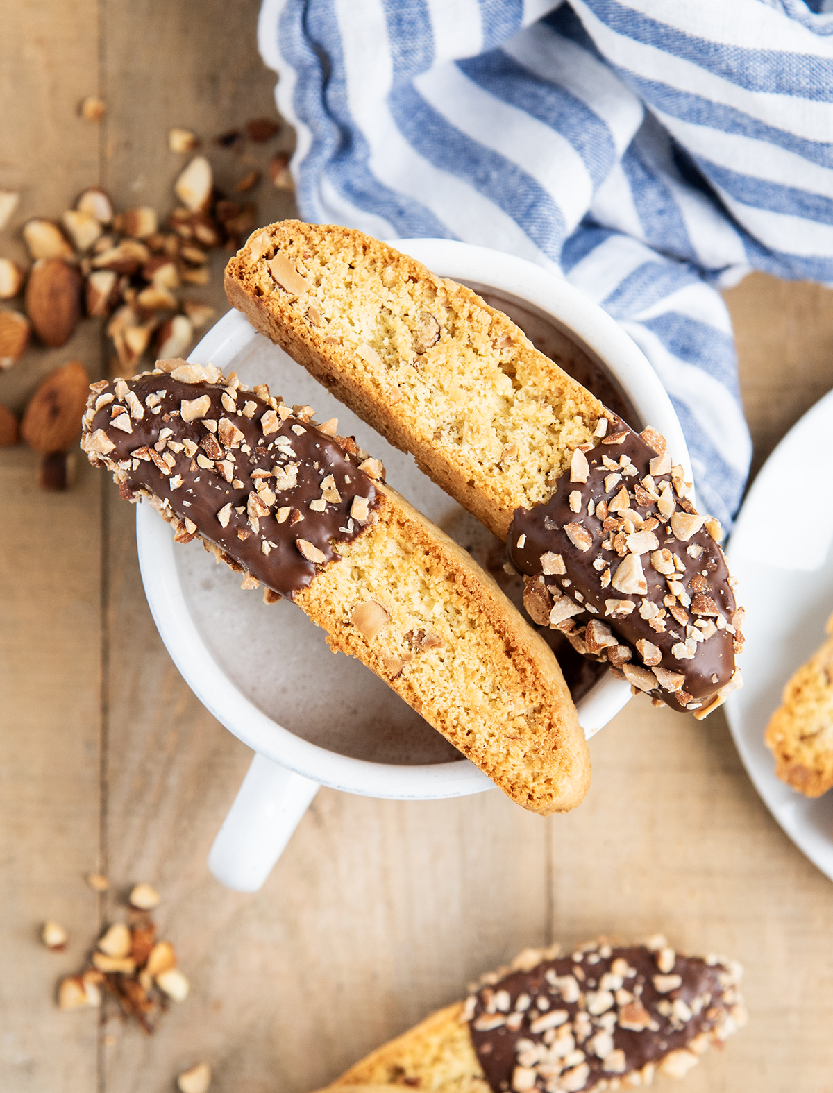Two chocolate dipped almond biscotti on a mug of coffee.