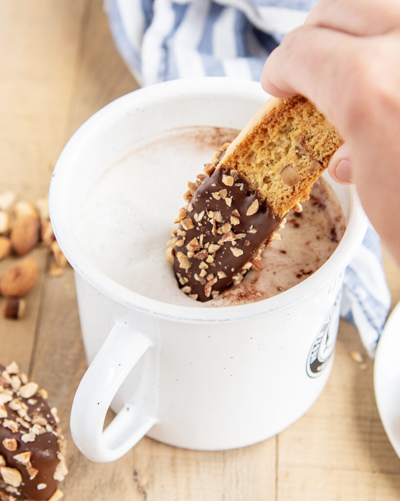 A hand dipping an almond biscotti cookie into a mug of coffee.