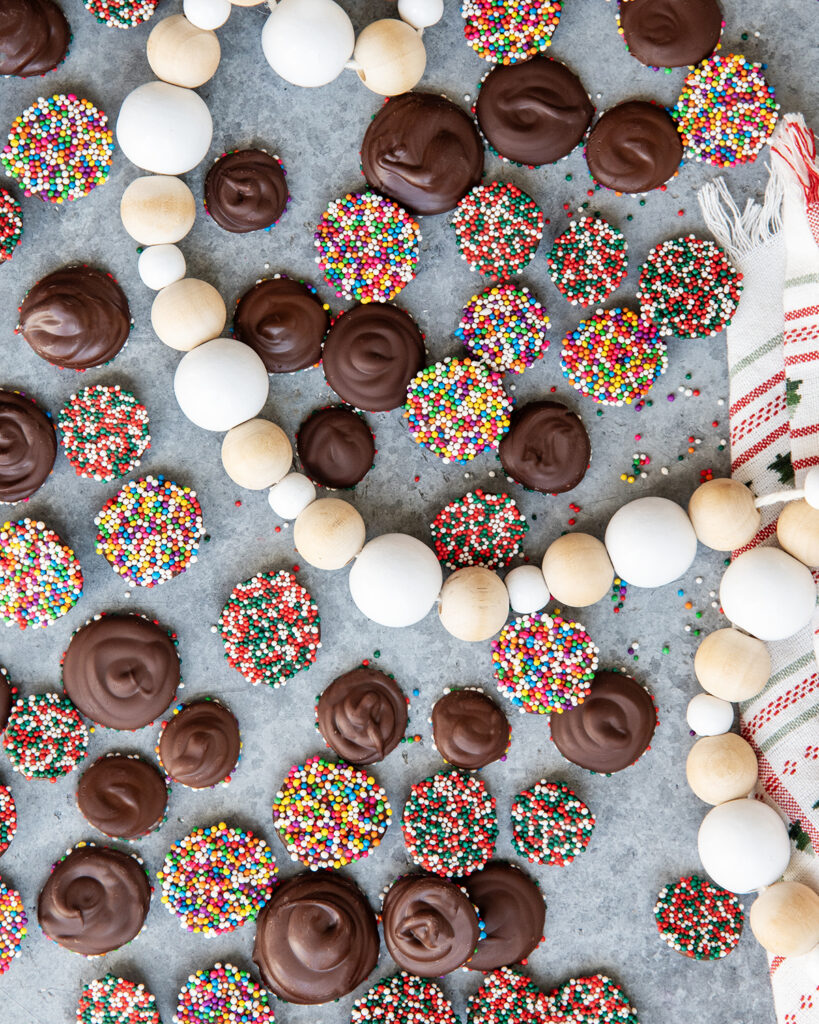 An above view of chocolate non pareils, some are showing the chocolate side, some are showing non pareil ball sprinkles.