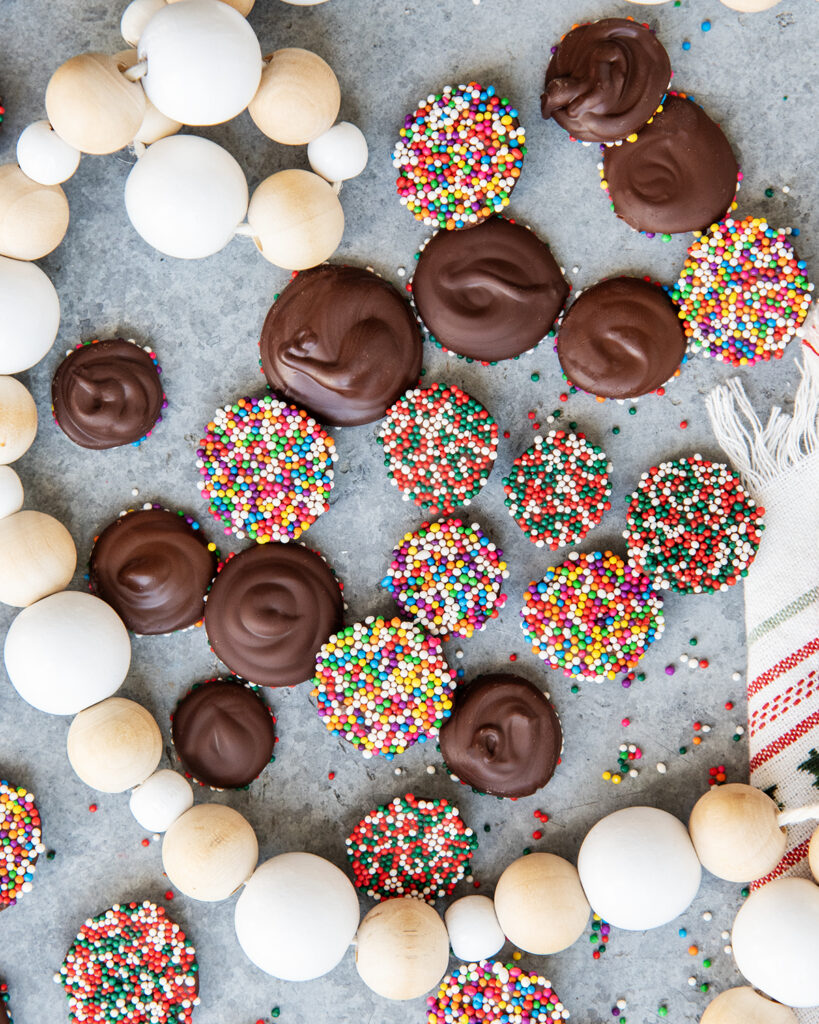 An above view of chocolate non pareils, some are showing the chocolate side, some are showing non pareil ball sprinkles.