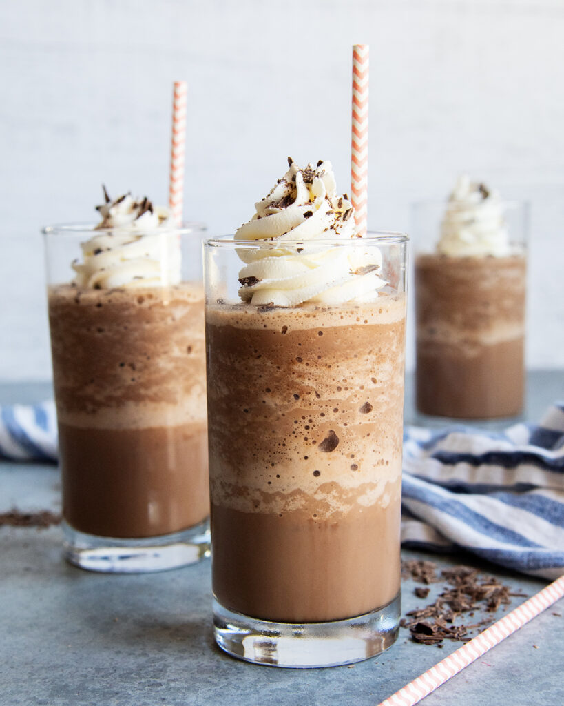 Three glasses full of frozen hot chocolate liquid, whipped cream, and straws.