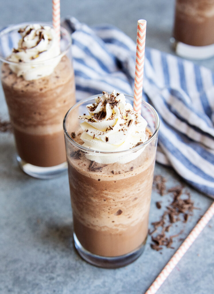 A glass of frozen hot chocolate liquid topped with whipped cream, chocolate syrup, and shavings.