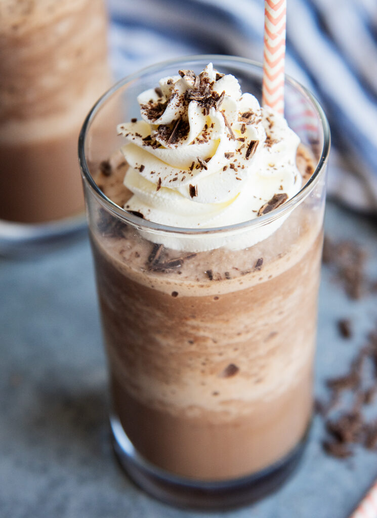 A glass of frozen hot chocolate liquid topped with whipped cream, chocolate syrup, and shavings.