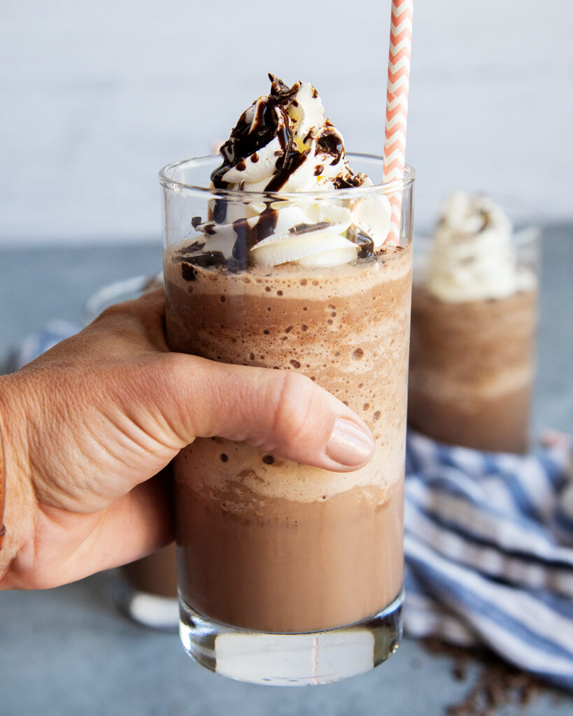 A hand holding a glass of frozen hot chocolate.