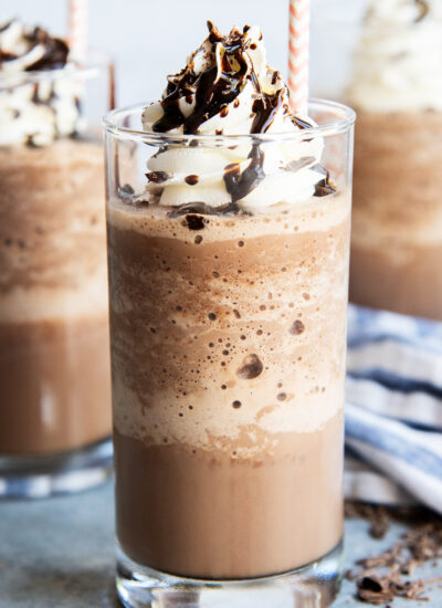 A glass of frozen hot chocolate liquid topped with whipped cream, chocolate syrup, and shavings.