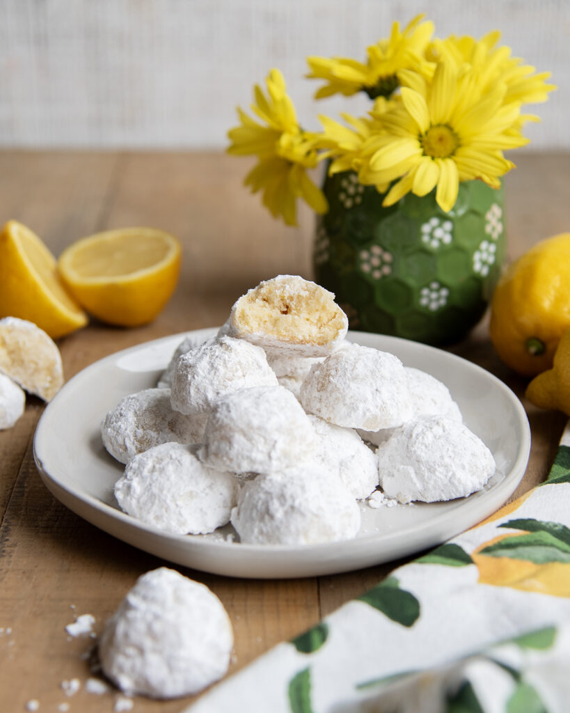 A plate of lemon snowball cookies, with one cookie bit in half showing the center of the cookie.