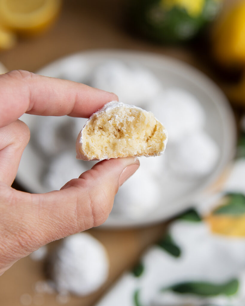 A hand holding half a lemon snowball cookie showing the center of it.