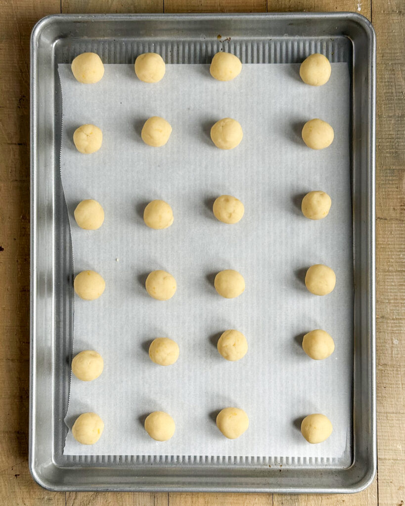 Small balls of snowball cookie dough on a cookie sheet.