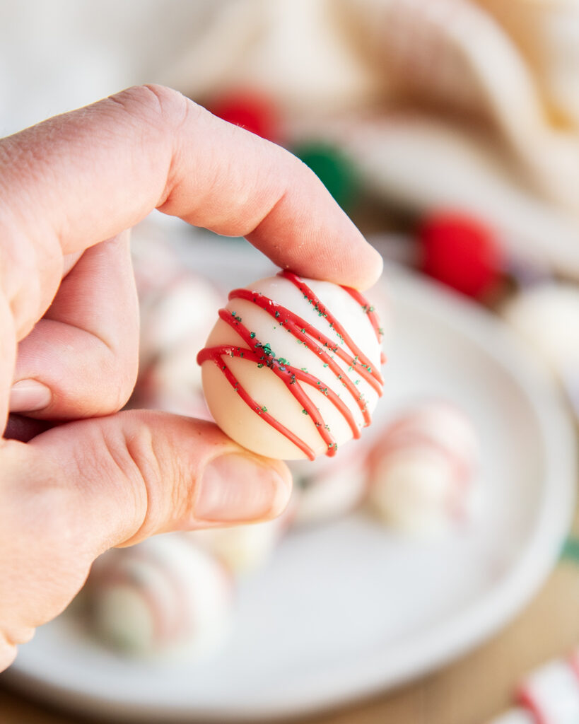 A hand holding a white chocolate dipped Little Debbie Christmas Tree Truffle.