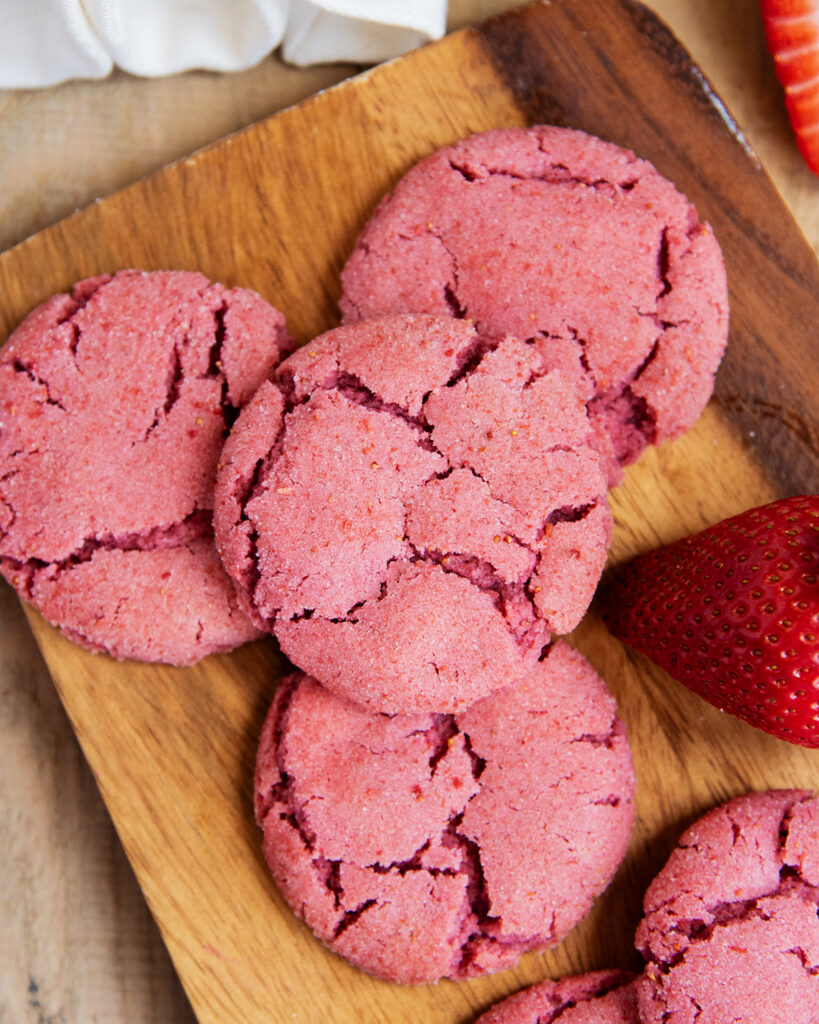 A wooden board topped with strawberry drop style sugar cookies.