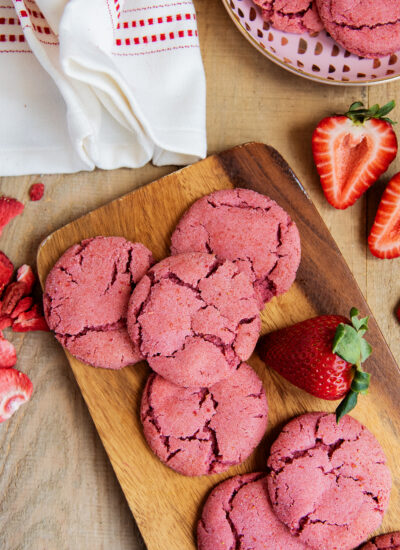 A wooden board topped with strawberry drop style sugar cookies.