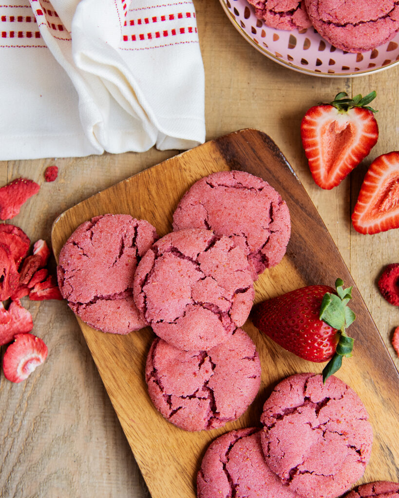 A wooden board topped with strawberry drop style sugar cookies. 