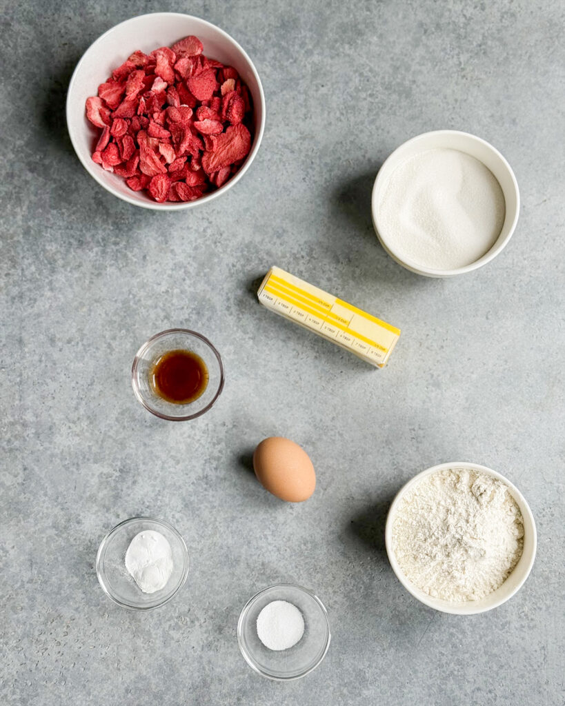 The ingredients needed to make strawberry sugar cookies, including butter, freeze dried strawberries, sugar, baking powder, baknig soda, and flour. 