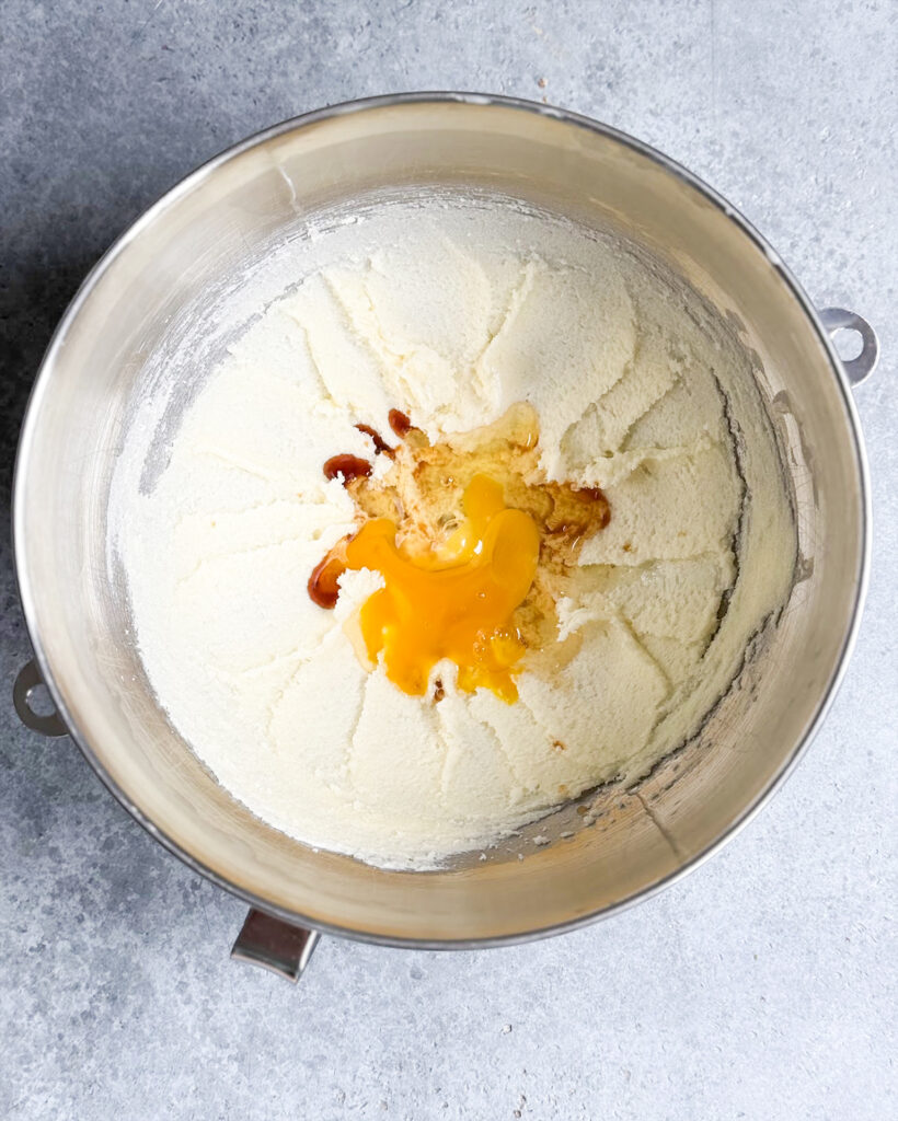 A bowl of creamed butter and sugar topped with vanilla and an egg.