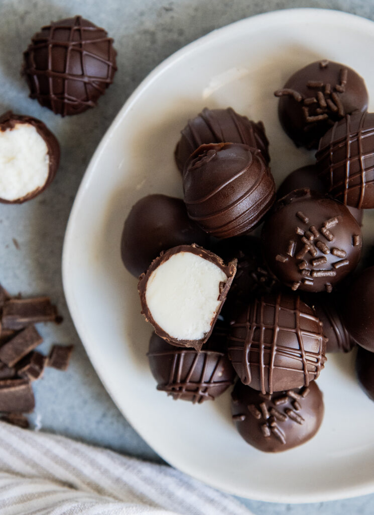 An above view of a plate of chocolate coated candies, and one is cut open showing a buttercream filling.