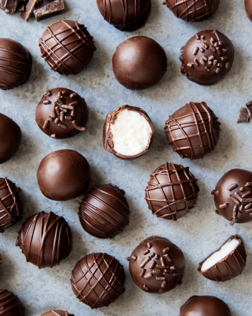 Chocolate coated Buttercream candies on a counter top, and one is showing the buttercream filling in the middle.