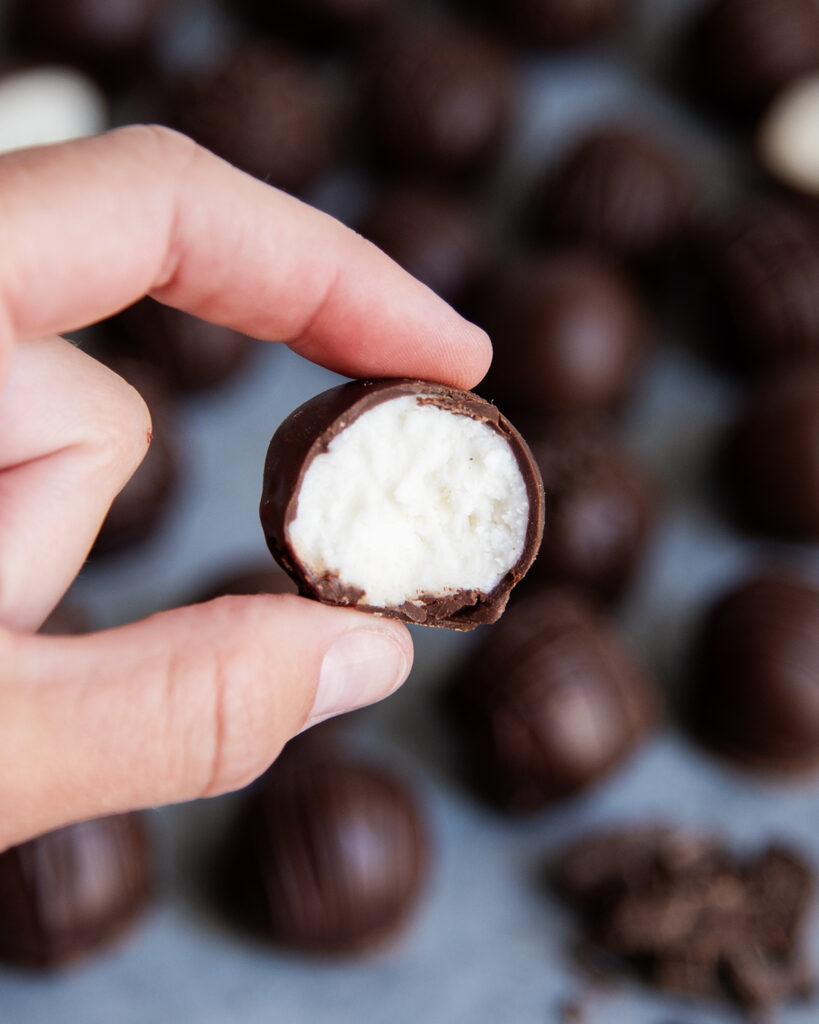 A hand holding a buttercream candy with a bite out of it with the white filling in the middle.