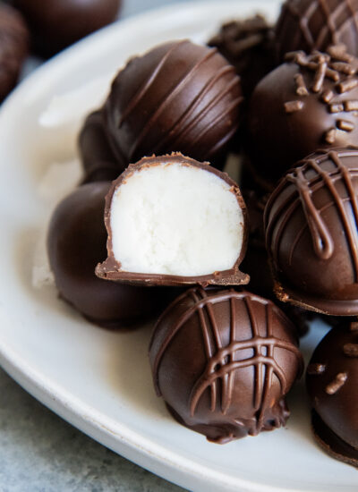 A plate of chocolate buttercream candies and one is cut in half showing the filling in the middle.