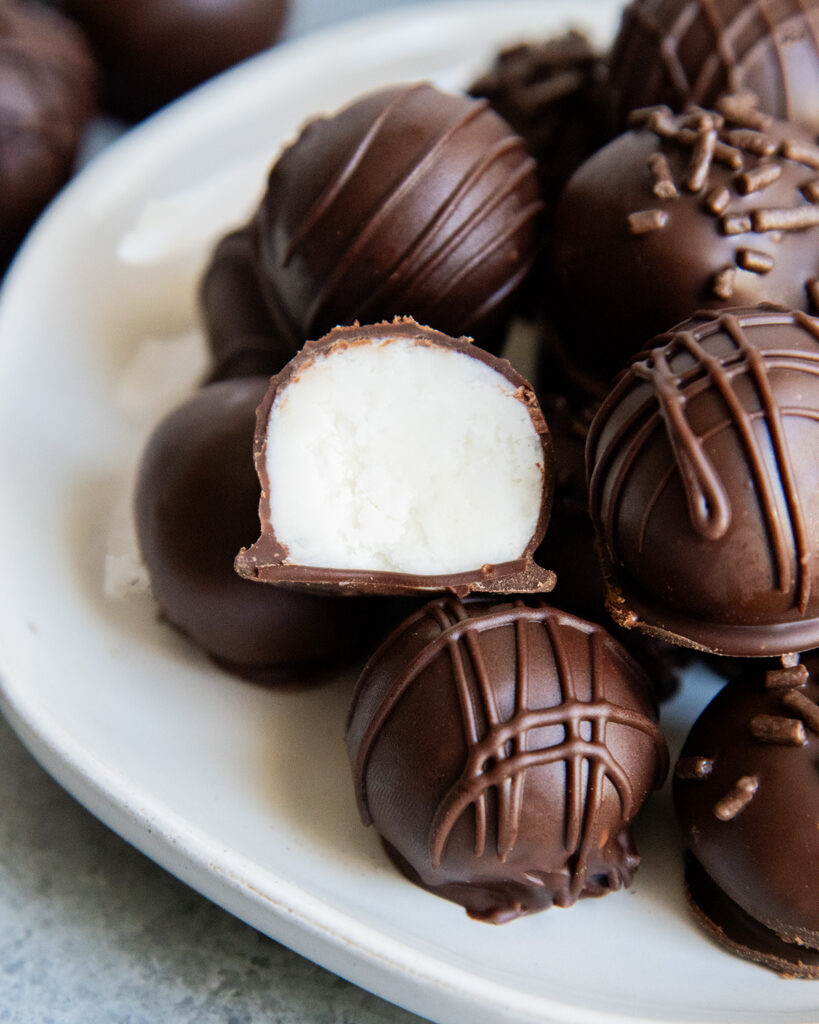 A plate of chocolate buttercream candies and one is cut in half showing the filling in the middle.