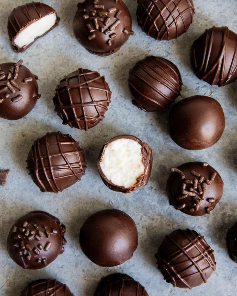 Chocolate coated Buttercream candies on a counter top, and one is showing the buttercream filling in the middle.