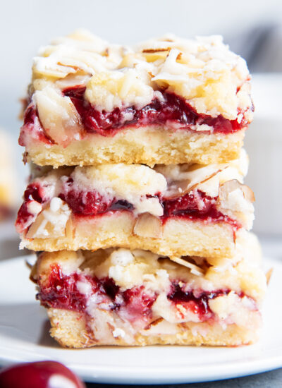A stack of three cherry cookie bars with slivered almonds and an almond glaze on top.