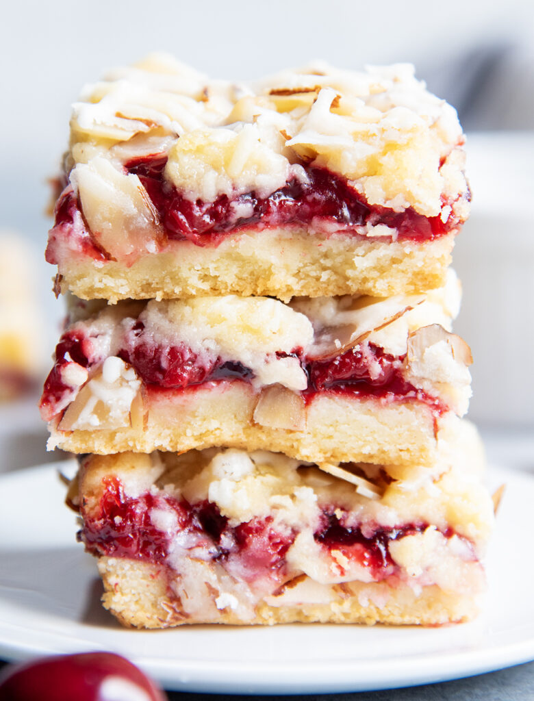 A stack of three cherry cookie bars with slivered almonds and an almond glaze on top.