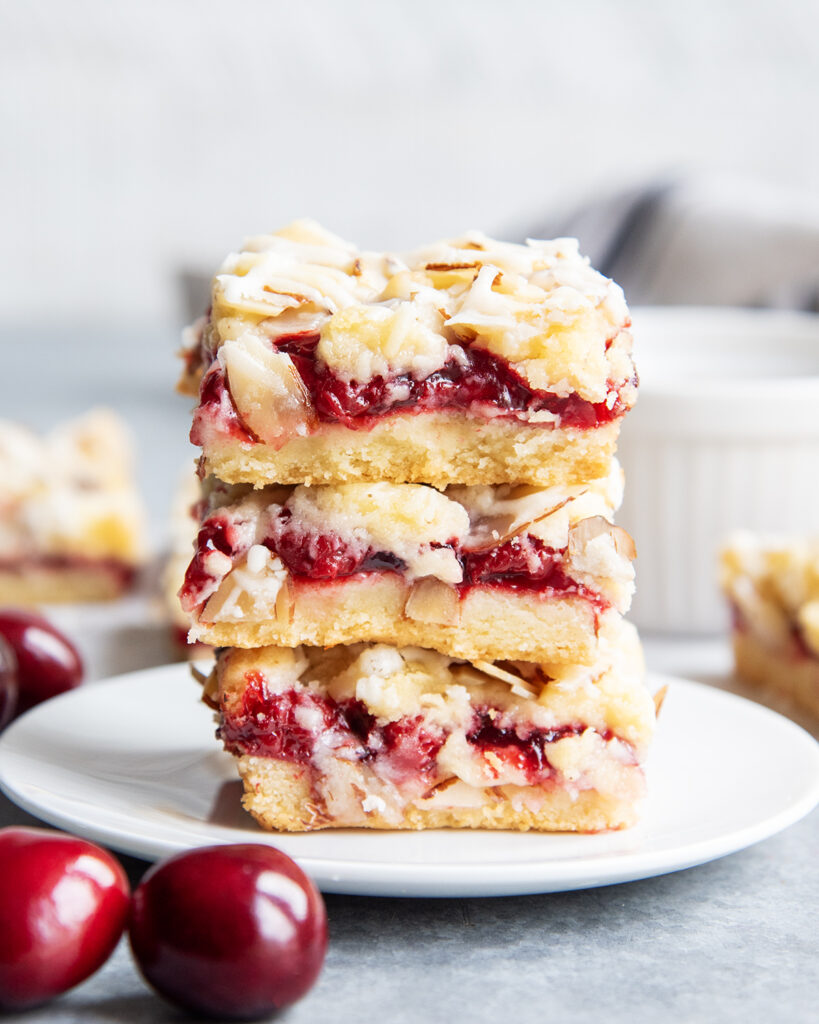 A stack of three cherry cookie bars with slivered almonds and an almond glaze on top.