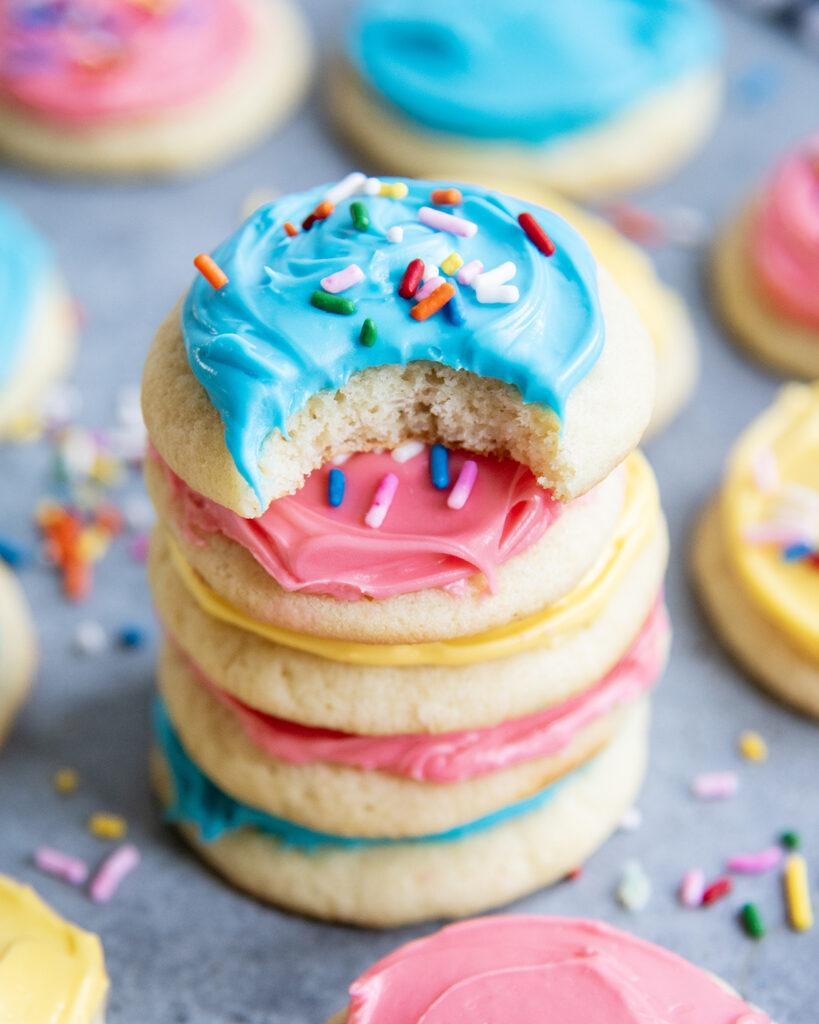 A stack of colorfully frosted sour cream sugar cookies and the top cookie has a bite out of it.