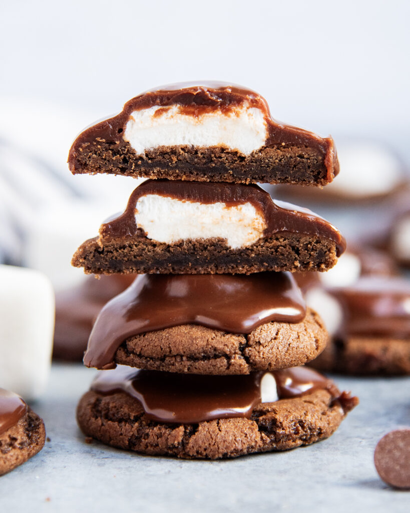 A stack of chocolate marshmallow cookies, the top two are cut in half showing the gooey marshmallow under the ganache.