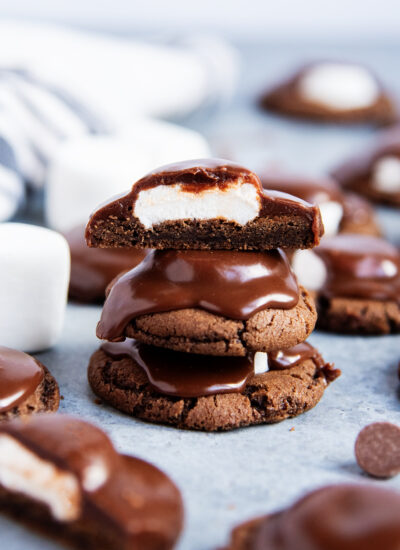 A stack of three chocolate ganache topped marshmallow chocolate cookies, the top cookie is cut in half showing the marshmallow center.
