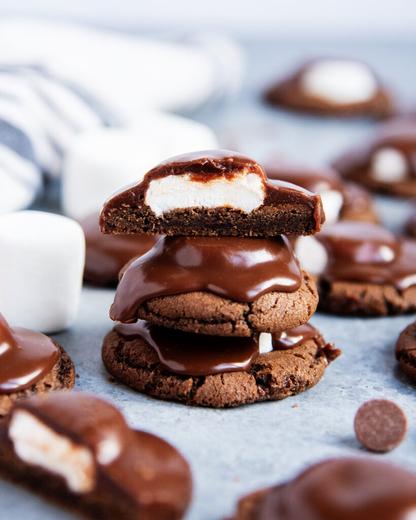 A stack of three chocolate ganache topped marshmallow chocolate cookies, the top cookie is cut in half showing the marshmallow center.