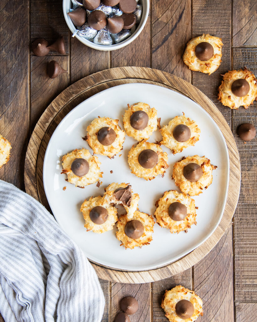 A plate of coconut macaroon cookies topped with hershey kisses. One cookie has a bite out of it.