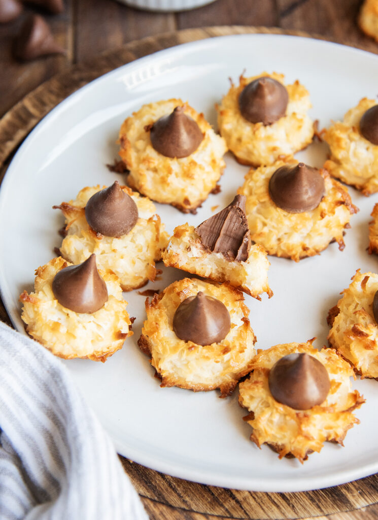 A plate of coconut macaroon cookies topped with hershey kisses. One cookie has a bite out of it.