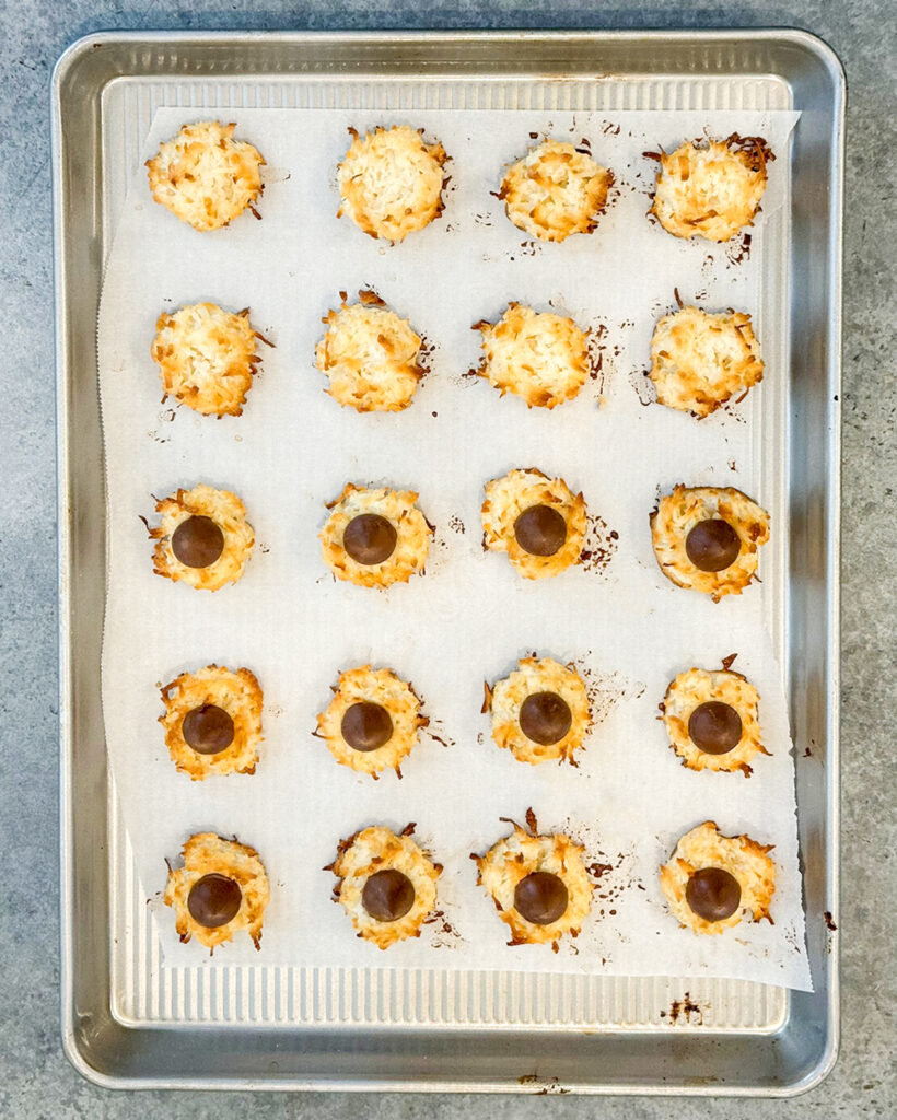 An above view of coconut macaroon cookies on a baking sheet, half of them are topped with a hersheys kiss.