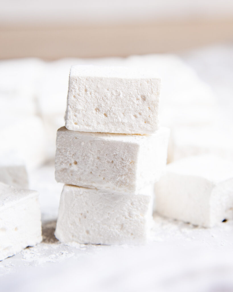 A stack of tree square vanilla marshmallows on a piece of parchment paper.