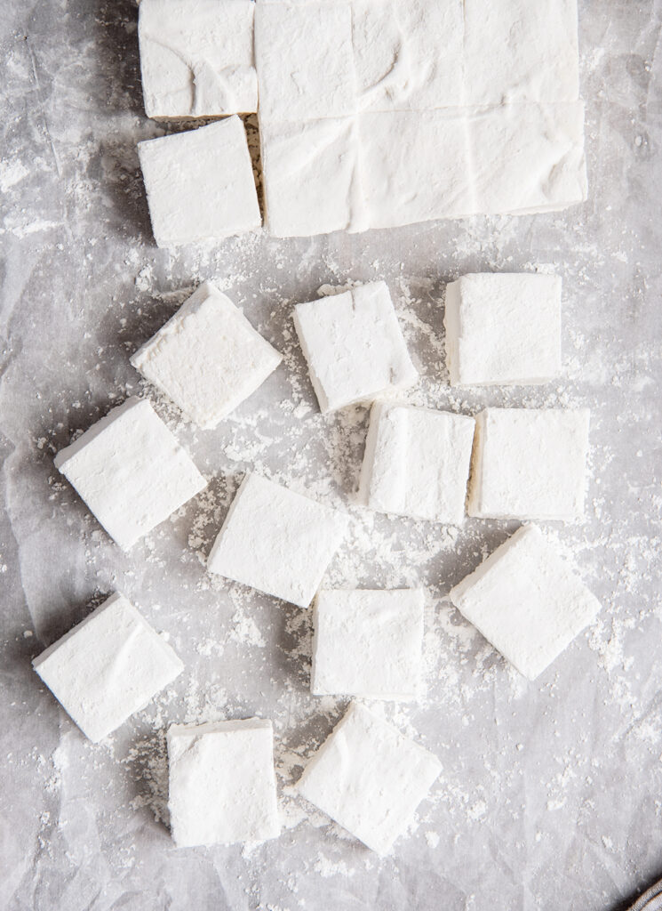 An above view of square homemade marshmallows on a piece of parchment paper.