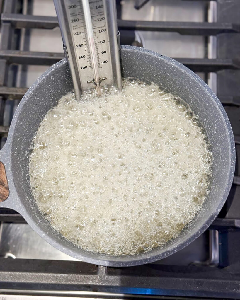 A boiling candy mixture in a pot with a candy thermometer.