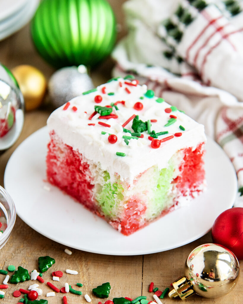 A plate of a slice of Christmas cake topped with Cool Whip, and full of red and green jello coloring.