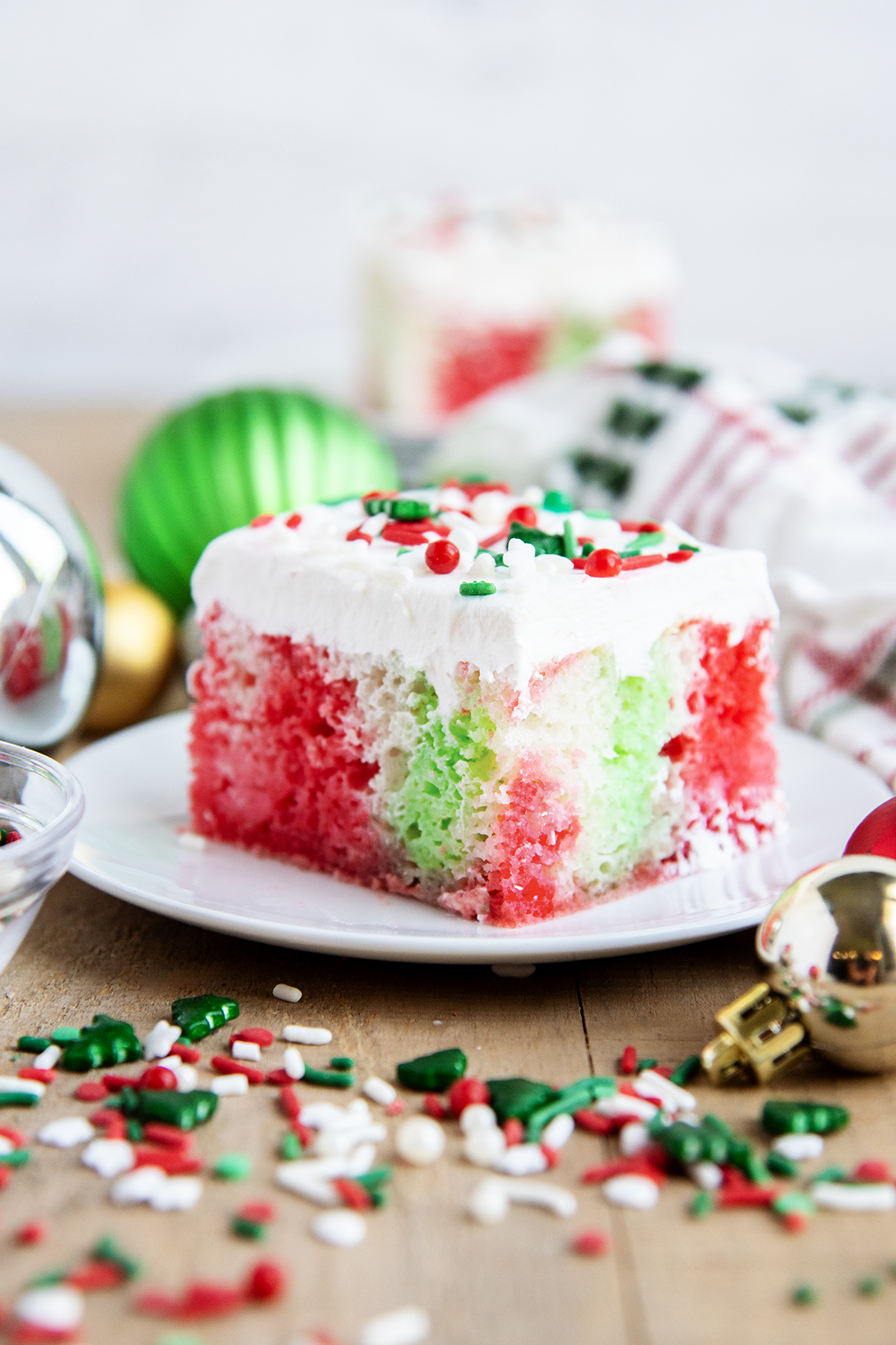 A plate of a slice of Christmas cake topped with Cool Whip, and full of red and green jello coloring.