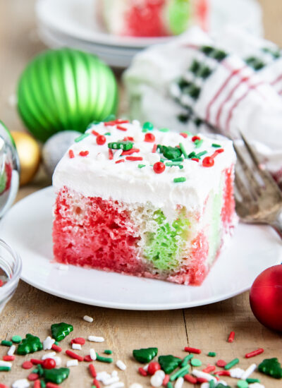 A plate of a slice of Christmas cake topped with Cool Whip, and full of red and green jello coloring.