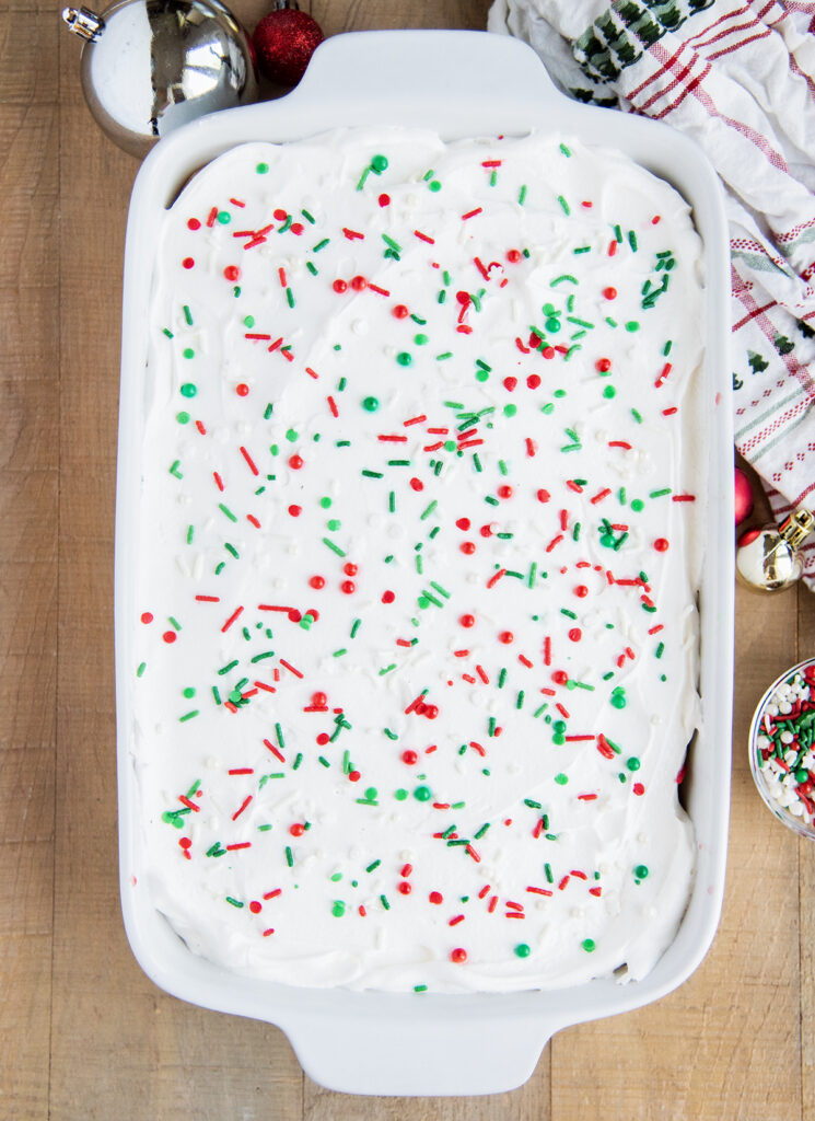 An above view of a pan of cake topped with cool whip and Christmas sprinkles.