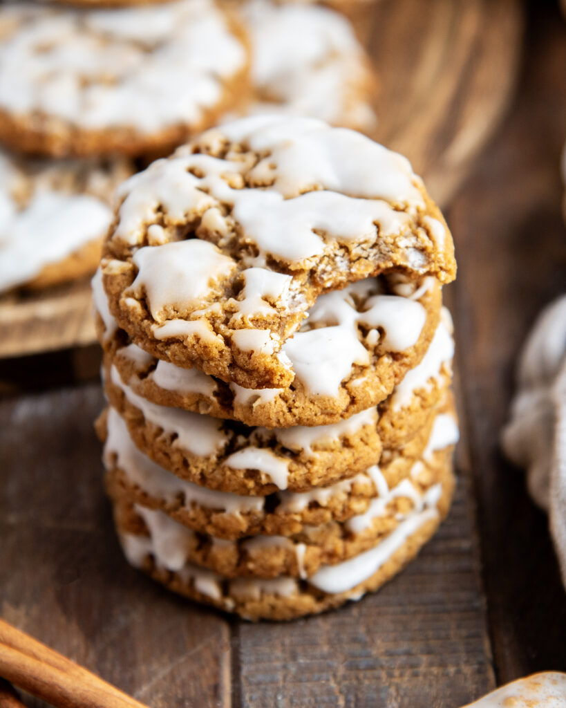 A stack of gingerbread oatmeal cookies, with icing on top, and the top cookies has a bite out of it.