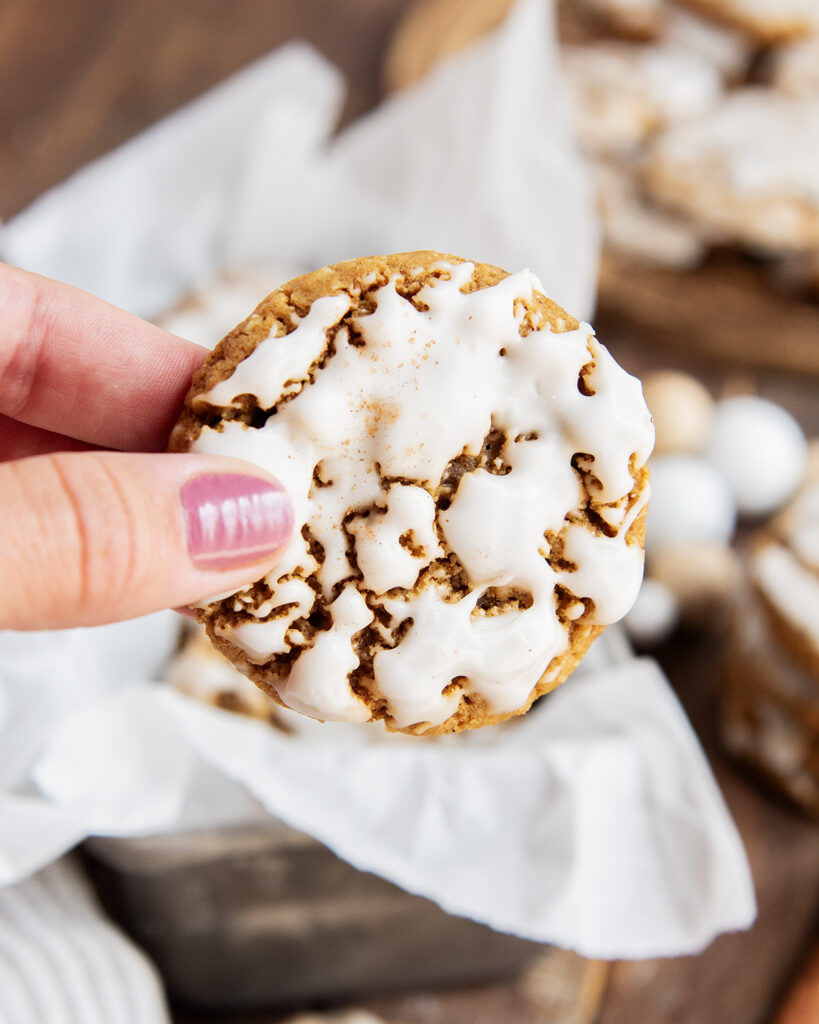 A hand holding an oatmeal cookie topped with a white icing.