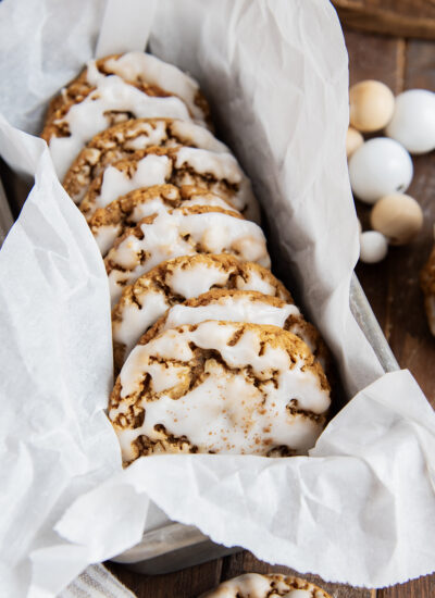 A side ways stack of iced gingerbread oatmeal cookies in a parchment paper lined tin.